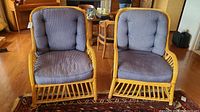 Two matching natural rattan chairs with blue padded cushions, side by side on a wood floor.