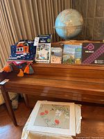 Lot contents on wooden piano surface showing world globe, travel books, two macrame tapestries.
