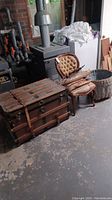 Photo of the lot showing wood steamer trunk, balloon back chair with tufted seat, large round basket, and a small decorative wooden boat.