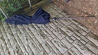 Folded navy blue outdoor umbrella with metal pole placed on outdoor ground.