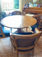 Photo showing round wooden table with brass base and 4 wooden cane back arm chairs with black cushions