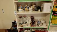 Full view of shelf with assorted figurines and glassware including Thomas Kincaid Angel of Faith light
