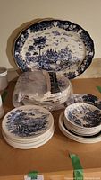 Photo showing an 18-inch platter, stacked plates including lunch and side plates, and small bowls all featuring blue countryside pattern underglaze decoration