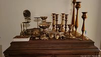 Overview of various brass and copper candlesticks, bells, and decorative items on wooden surface
