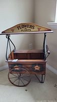 Front view of the wooden planter cart with 'FLOWERS & PLANTS' sign and floral painted decoration.