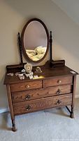 Full view of vintage wooden dresser with oval mirror, two small top drawers, three large bottom drawers, and decorative items on top.