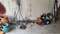 Black metal garden plant frames with decorative floral design, wire plant cages, assorted pots, and solar garden lights arranged on the ground