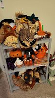 Front view of resin 3-shelf unit filled with various Halloween decorations including scarecrows, pumpkin buckets, and candles.