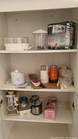 Shelf with various kitchen appliances including Braun Multimix mixer box, Salton yogurt maker, meat grinder, coffee grinders, and kitchen tools