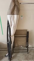 Umbrella folded up with beige and white fabric cover and folded chair behind it.