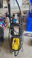 Photo of the yellow Karcher K 360 power washer on a concrete floor with hose loosely coiled and handle visible.