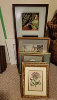 Various framed prints leaning against wall showing floral and architectural subjects.