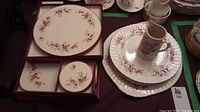 Photo of lavender rose patterned large round plate, smaller round plates, rectangular plates, and coasters in their boxes.