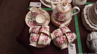 Overview of 8 teacups, 8 saucers, 8 side plates, creamer, sugar bowl and teapot on table.