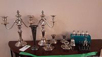 Two silver-plated three-arm candelabras, silver vase, multiple candle holders, and two sets of Birks sterling salt and pepper shakers in blue boxes on a wooden surface