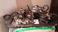 Photo showing full silver plated tea set on large ornate tray including teapot, sugar bowl, creamer, salt and pepper shakers, and tea strainers.