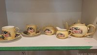 Full view of the tea set arranged on a shelf showing all 6 pieces including teapot, sugar bowl, creamer, and two cups with saucers.