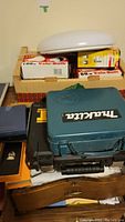 Photo showing Makita electric drill case, boxes of Valu-Bulb light bulbs, and ceiling light fixture on table.