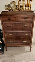 Front view of the vintage dresser showing five drawers with brass handles and decorative legs.