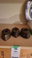 Three vintage heavy metal irons shown base side up, triangular shape with vent holes and solid metal construction.