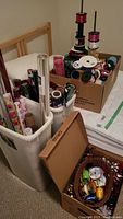 Two boxes and two bins filled with ribbons and wrapping paper placed on a bed and floor