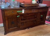 Front view of dark stained wood buffet with 3 drawers in center and 2 doors each with carved shell accent