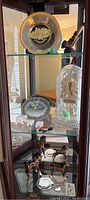 Shelf view of all items including glass domed clock, geode clock, ceramic ponies, stone turtle, polar bears, souvenir plate, and smoking pipe