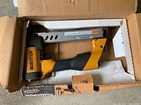 The full stapler inside a cardboard box, showing the overall shape, color and packaging.