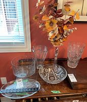 View of multiple crystal and glass items on wooden surface by window including vases, bowls, platter