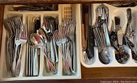 Top drawer divided tray with stainless steel forks, spoons, and knives arranged neatly.