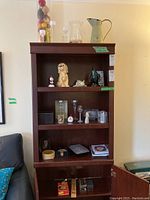 Full view of dark wood cabinet with shelves holding figurines, glassware, books, and games.
