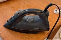 Proctor Silex electric iron showing side profile, black color, power cord attached, temperature dial visible