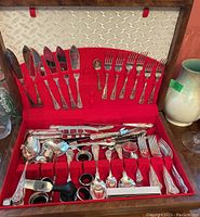Full view of silverware collection arranged in red velvet-lined wooden box showing knives, forks, spoons, serving utensils, wine collars, and napkin rings.