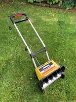 Full view of Noma snow thrower on grass, showing handle, controls, and body with Noma label.