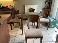 Photo showing round wood dining table with glass top and four matching chairs with upholstered seats arranged around it.
