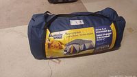 Blue carry bag with large yellow label showing the tent brand, model, and capacity for 13 people.