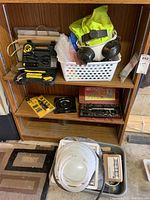 Image of wooden shelf unit displaying varied hand tools including Fixman tool kit, ratchet socket set, safety supplies like respirator mask and high visibility vests, and miscellaneous white tubing and black parts below shelf.