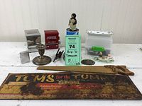 Lot of vintage items on table including toothpick dispensers, candlestick, saw blades, figurines, advertising sign, and other collectibles.