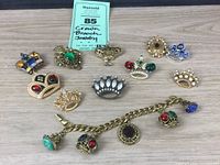 All items of the lot displayed on wooden surface, including 10 crown-themed brooches and a gold-tone charm bracelet with 5 crown charms.