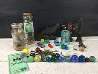 Full lot overview showing vintage bottles including Green Spot, glass marbles spread out, metal keys, and small toys in front of black background on white surface.