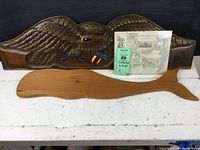Wooden carved eagle plaque, wooden whale shape, and Cape Cod railroad map shown together on table