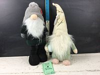 Pair of gnome figurines, one dressed in dark green and gray winter attire with knit hat, the other in pastel spring colors with tall hat.