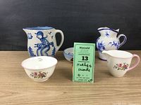 Group photo of the six pottery pieces including pitchers, bowls, and sugar set on a wooden surface against a dark background