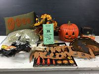 Overall photo showing the assembled Halloween decor items on a white wooden surface including the ceramic pumpkin, fall flower arrangement, 'Boo!' pillow, pumpkin carving tools and decorations.