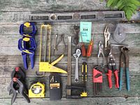 Full set of assorted used hand tools on weathered wood surface including clamps, caulking gun, pliers, screwdrivers, wrenches, and measuring tools.
