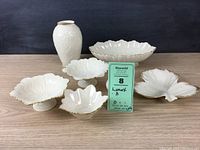 Seven-piece Lenox China collection including candy dishes, various dishes, oval bowl and two vases, all white with gold trim and embossed floral patterns.