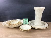 Eight pieces of white Lenox porcelain including vase, bowls, candy dishes, and platters, arranged on wooden surface with black backdrop.