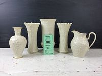 All five pieces including four Lenox vases with raised foliate designs and one milk pitcher with bramble fruit relief seen together on a white rustic table against black background.