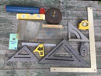Wide view of various measuring and leveling tools arranged on weathered wooden surface showing condition and assortment.