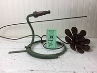 Two pieces of yard decor displayed on white surface: a rusted iron flower and a painted iron hose snake that holds a flower pot.